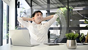 Relaxed Asian businessman putting his arms behind his head to relax after finishing work