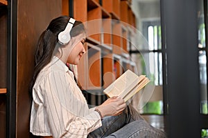 Relaxed Asian female in a bookstore listening to music while focused on reading a book