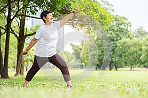 Relaxed Asian Senior woman in white cloth doing stretching workout her arms at park. Smiling Elderly Thai Female enjoying