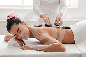 Relaxed asian woman enjoying hot stones back massage in spa salon