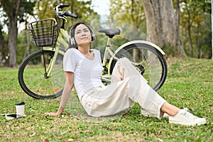 Relaxed Asian woman listening to music and taking a rest after cycling in the public park