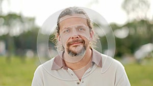 A relaxed attractive middle aged man with long gray hair looks into the camera, smiles and laughs.