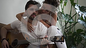 Relaxed bearded man playing guitar for his female lover at the bedroom at home Spbd. married
