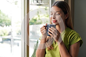 Relaxed beautiful young woman smelling her herbal tea at home in the morning