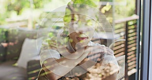 Relaxed biracial woman sitting on sofa looking outside, seen through window