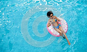 Relaxed black lady floating on inflatable ring and enjoying her cocktail drink at pool, top view. Space for text