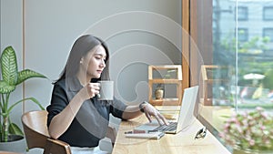 Relaxed business woman drinking coffee and checking email on her laptop computer.
