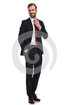 Relaxed businessman fixes his red tie and looks to side