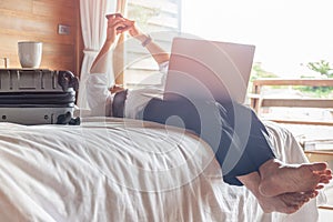 Relaxed businessman lying in bed looking at cellphone with laptop on his lap.