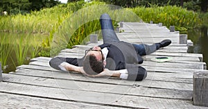 Relaxed businessman lying on wooden bridge in green park