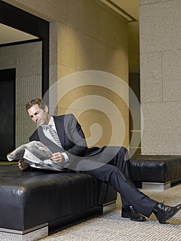 Relaxed Businessman Reading Newspaper In Office Lobby