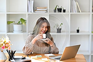 Relaxed businesswoman drinking coffee and reading email on her laptop computer.