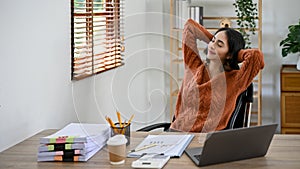 Relaxed Asian businesswoman resting at her desk, eyes closed, leaning on her chair