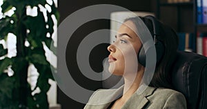 Relaxed calm woman sitting at table relaxing listening to music wearing wireless headphones talking nline dream job work