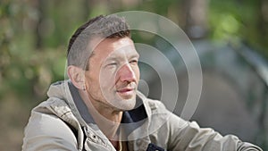 Relaxed Caucasian man in sunshine looking away enjoying calm leisure in forest camp. Close-up portrait of satisfied