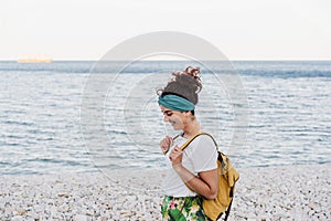 Relaxed caucasian woman with yellow backpack walking by the beach during sunset. summer time. daydreaming. Outdoors lifestyle