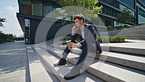 Relaxed ceo talking mobile phone sitting urban stairs with coffee cup zoom in.