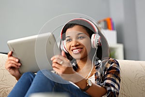 Relaxed charming african american woman in headphones listening to music and choosing with finger on tablet screen