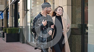 Relaxed cheerful gay man and young woman talking strolling on city street arm in arm. Dolly shot portrait of positive