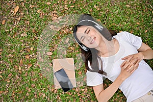 Relaxed and chilling young Asian woman listening to music , smiling, eyes closed and lying on grass