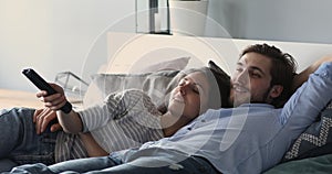 Relaxed couple lying in bed holding remote control watching tv