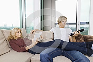 Relaxed couple reading book and watching TV in living room at home