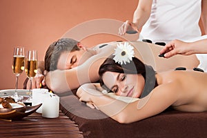 Relaxed couple receiving hot stone therapy at spa