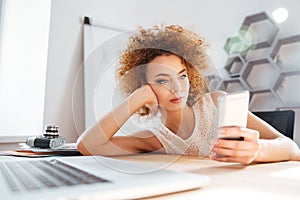 Relaxed cute curly young woman using mobile phone in office