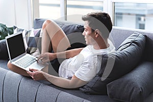 Relaxed cute guy is typing on keyboard of modern device