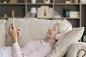 Relaxed elder smartphone user woman in headphones listening to music