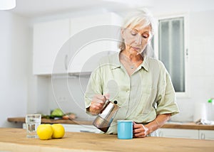 Relaxed elderly woman drinking coffee at kitchen