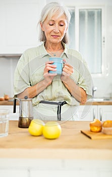 Relaxed elderly woman drinking coffee at kitchen