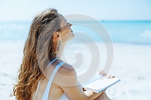 relaxed elegant woman on seacoast with straw bag and book