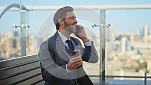 Relaxed entrepreneur talking mobile phone on terrace. Happy bearded man speaking