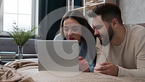 Relaxed family couple in love lying on bed with laptop shopping online choose delivery store Caucasian woman man buying