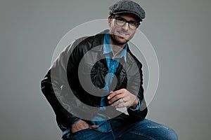 Relaxed fashion man wearing leather jacket and flat cap sitting