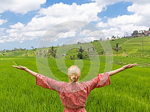 Relaxed fashionable caucasian woman wearing red asian style kimono, arms rised to sky, enjoying pure nature of beautiful