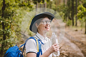 Relaxed female tourist resting in nature. Happy woman tourist with backpack. tourist girl drinking water in forest. Female with