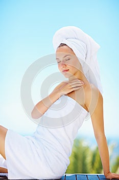 Relaxed female wrapped in a towel sitting against the blue sky. Young woman after a bath sitting against the sky with