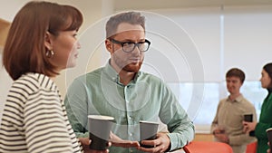 Relaxed friendly coworkers standing in office, drinking coffee and talking cheerfully in office room during break. Male