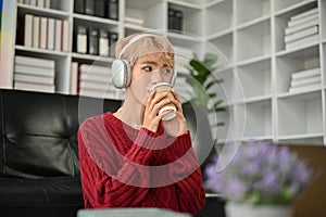 A relaxed gay man is enjoying the music on his headphones and sipping coffee in his living room