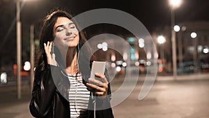 Relaxed girl enjoying music in earphones, walking in night city