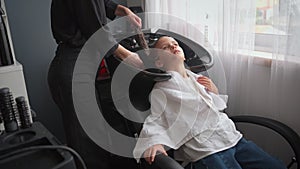 Relaxed girl having her hair washed by female hairdresser in salon