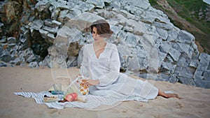 Relaxed girl pouring juice on beach picnic. Romantic woman enjoying weekend