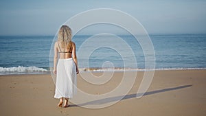 Relaxed girl stepping sand beach relaxing at evening sunlight back view.