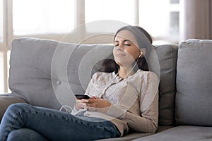 Relaxed girl wearing earphones listening to music playing via smartphone