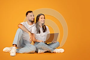 Relaxed and happy couple in white tops and blue jeans sitting cross-legged on the floor while sharing a laptop