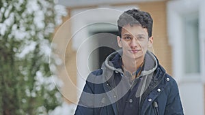 Relaxed happy Middle Eastern teenager standing outdoors on snowy day looking at camera and smiling. Portrait of joyful