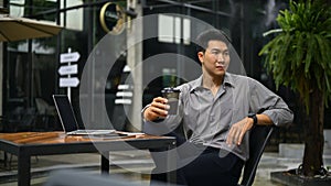 Relaxed businessman sits at a coffee shop in an outdoor space with his coffee in his hand