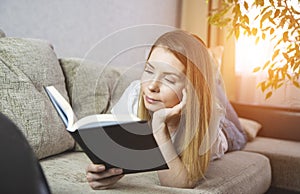 Relaxed happy woman reading a book in an ebook reader sitting on a couch at home